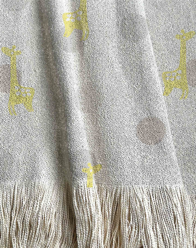 Manta tejida con diseño infantil, círculos tipo lunares en tonos grises y jirafas vectoriales amarillas.