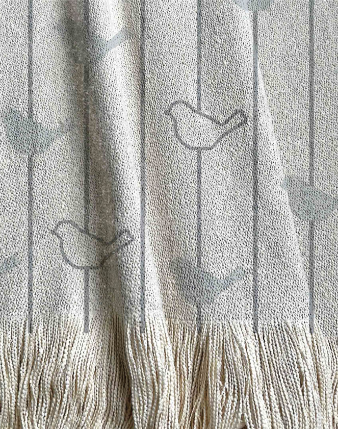 Manta tejida con diseño infantil. Pájaros y lineas en tonalidades grises.