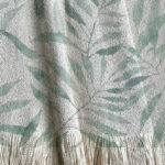 Manta tejida con diseño botánico, hojas aqua pintadas en acuarela.
