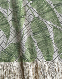 Manta tejida con diseño botánico, hojas de plátano en acuarela. Fondo geométrico de triángulos tipo montañas en tonos grises.